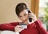 Young woman relaxing at home on the phone with credit card